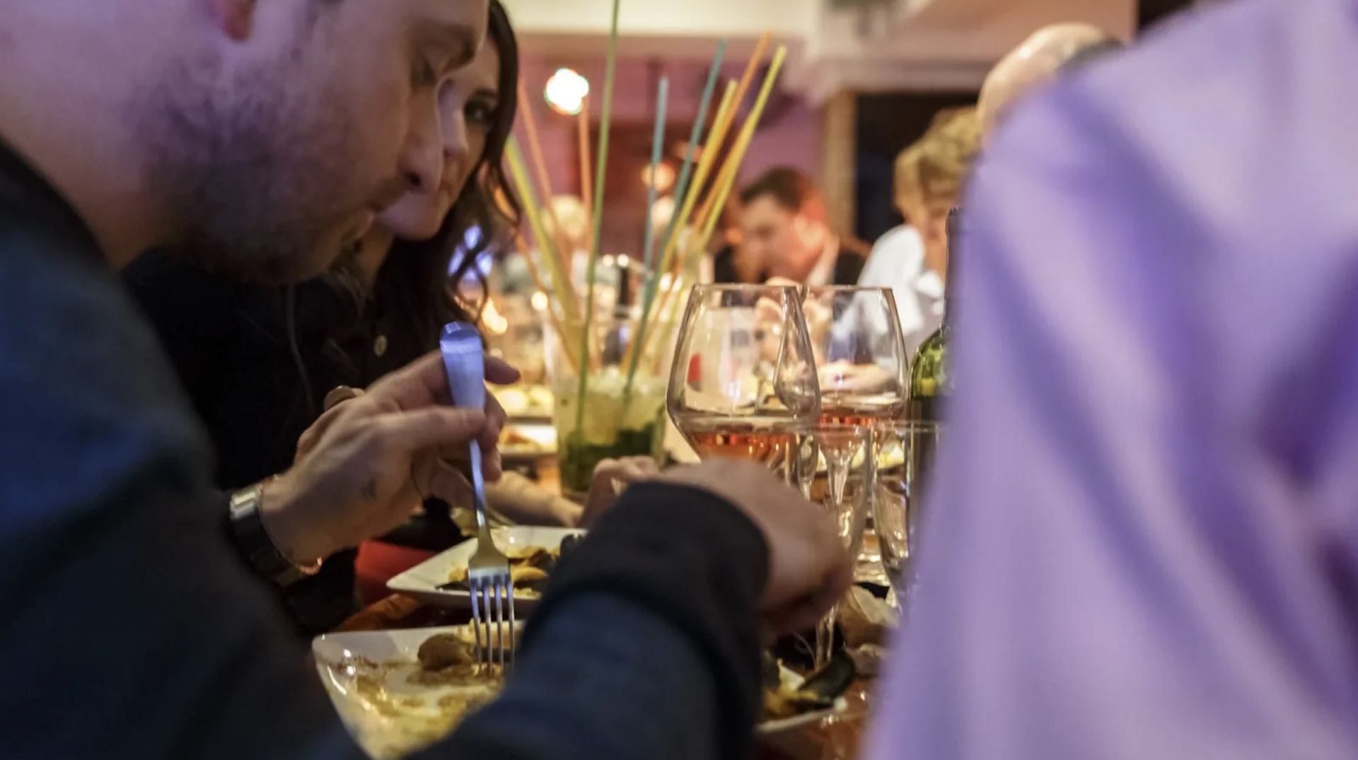 Grupo de personas disfrutando de una cena en un restaurante elegante con decoración dorada, copas de vino y ambiente cálido