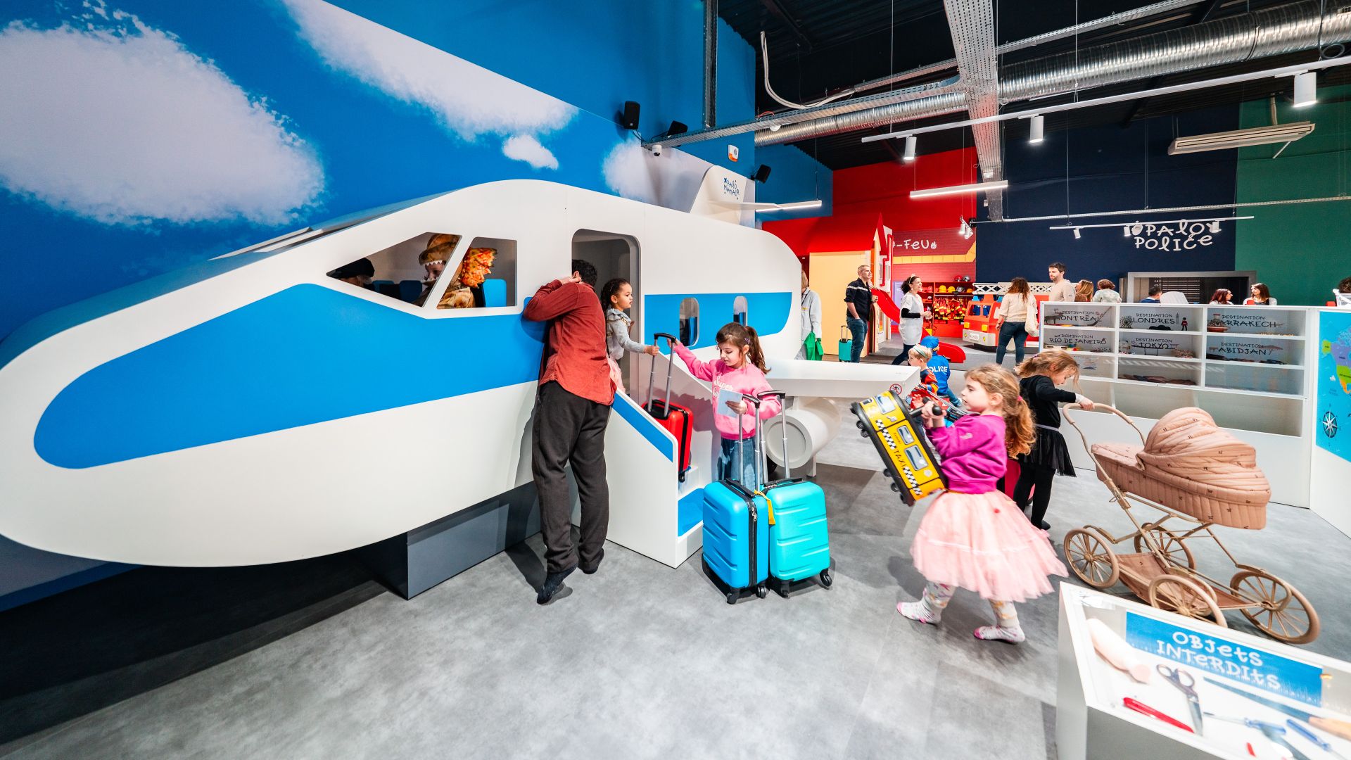 Niños interactuando con una exposición interactiva de un avión en un museo de Burdeos, con maletas de viaje y otros objetos decorativos temáticos.