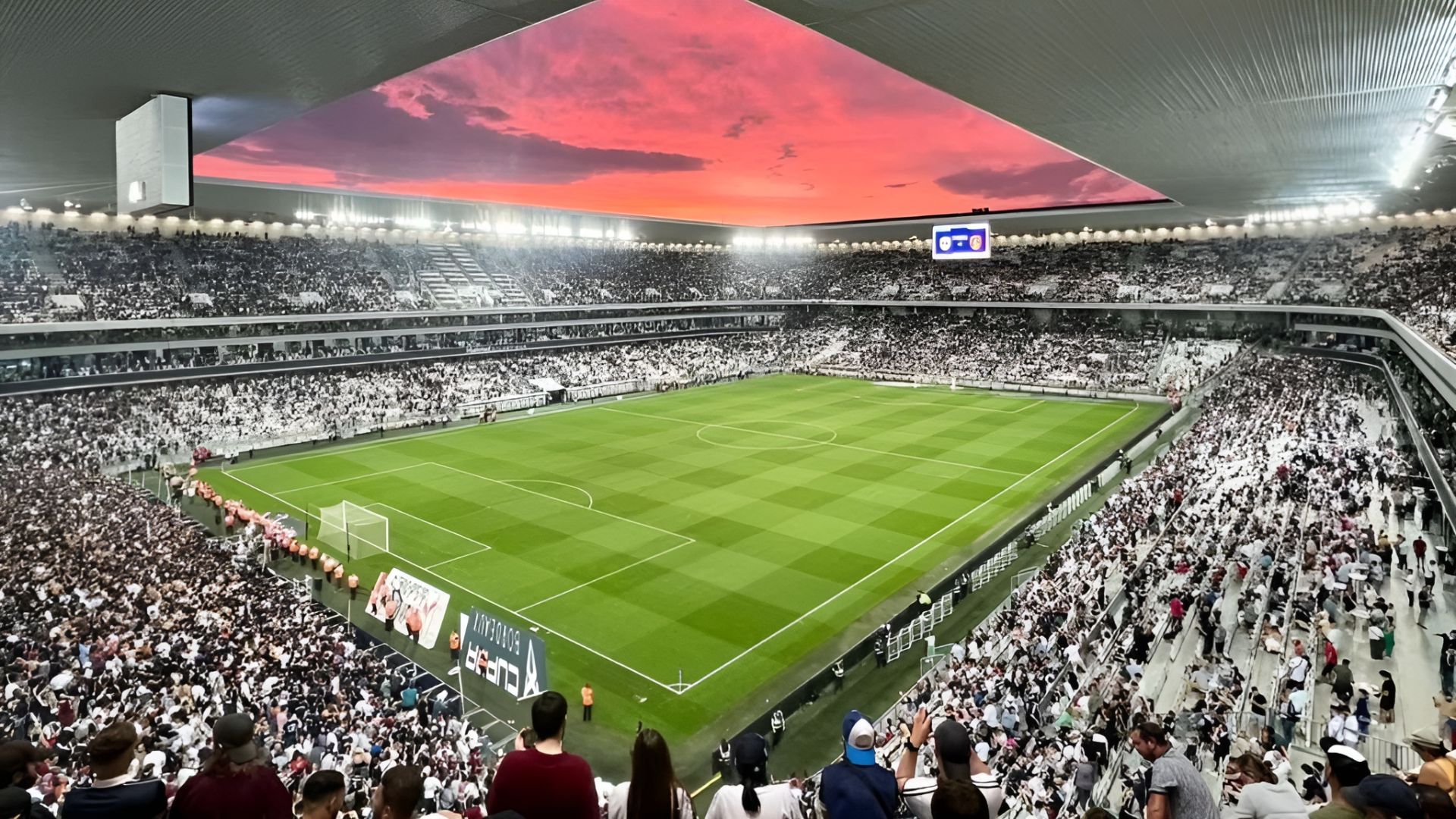 Vista interior del Estadio Atlántico de Burdeos lleno de espectadores durante un partido de rugby, con el campo de juego en verde y un cielo rojo al atardecer visible en la pantalla gigante del techo retráctil.