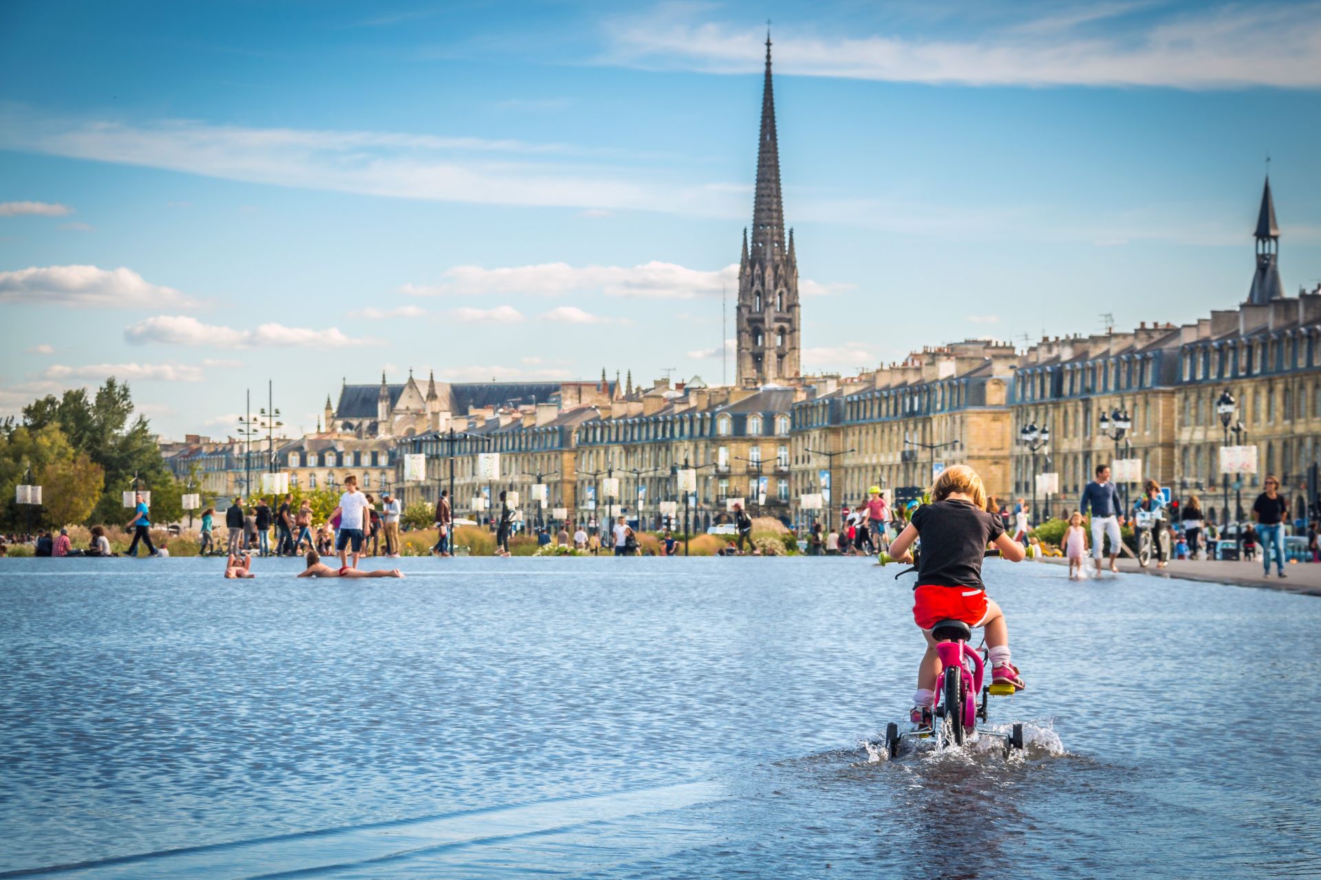 Cette photo met en avant une jeune fille en train de faire de vélo à roulettes sur le miroir d'eau.