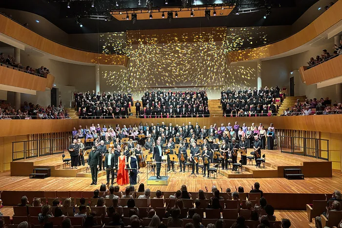 Concierto del coro sinfónico Viva Vivaldi en Burdeos con orquesta y cantantes en el escenario, público en balcones y platea de la sala de conciertos.