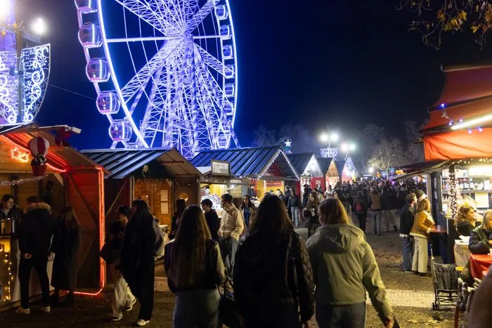 Mercado navideño de Burdeos por la noche con una noria iluminada en azul, casetas decoradas y visitantes pasando entre los puestos