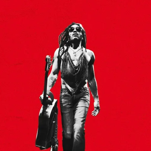 Lenny Kravitz en concierto en el Arkéa Arena de Burdeos, con gafas de sol y sosteniendo una guitarra sobre fondo rojo brillante.