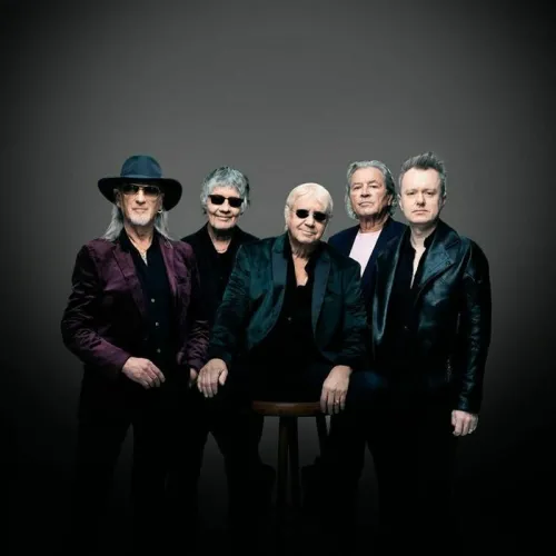 Retrato grupal de cinco músicos de Deep Purple con atuendos negros de escena y accesorios, posando sobre fondo gris.
