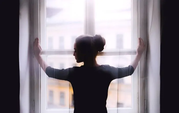Silueta de una mujer de espaldas con los brazos extendidos, mirando por una gran ventana con vistas a la ciudad de Burdeos