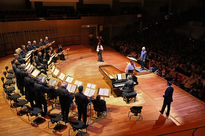 Representación del Barbero de Sevilla en Burdeos con una orquesta dispuesta en semicírculo, cantantes solistas en el centro y público sentado alrededor en una sala de conciertos.