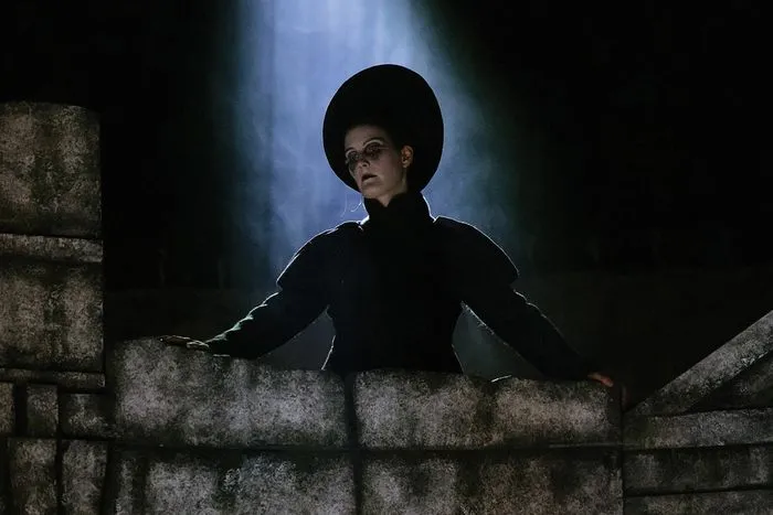 Actriz en traje negro sobre una muralla de piedra, iluminada por una luz azul dramática, en una producción de Dido y Eneas en la Ópera de Burdeos.