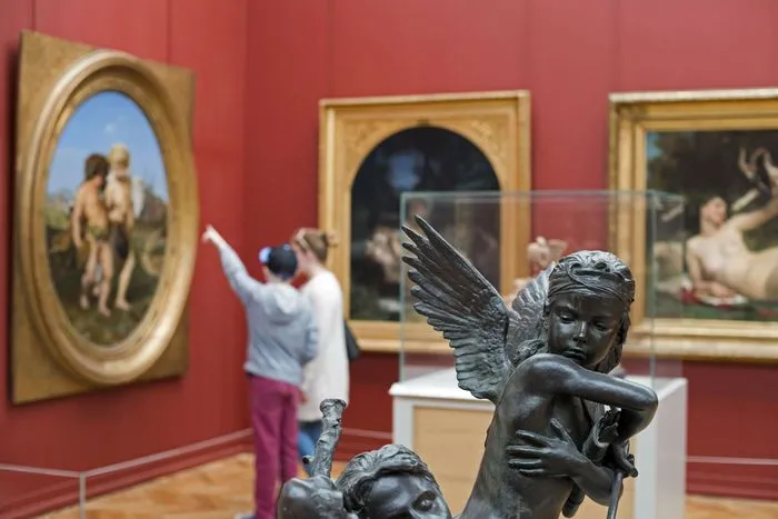 Interior del Museo de Bellas Artes de Burdeos con una escultura de ángel en bronce en primer plano y una visitante fotografiando cuadros en las paredes rojas.