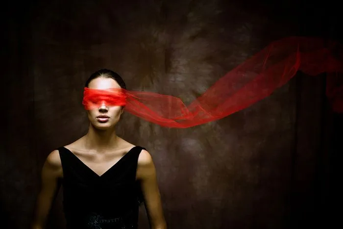 Mujer con los ojos vendados con tela roja ondeante, vestida de negro sobre fondo oscuro, evocando la ópera La Novia del Zar de Burdeos