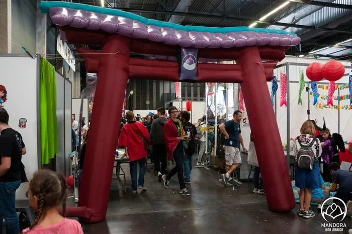 Entrada en forma de puerta torii roja en el festival Animasia de Burdeos, con visitantes pasando bajo la estructura decorada con linternas en una sala de exposiciones.