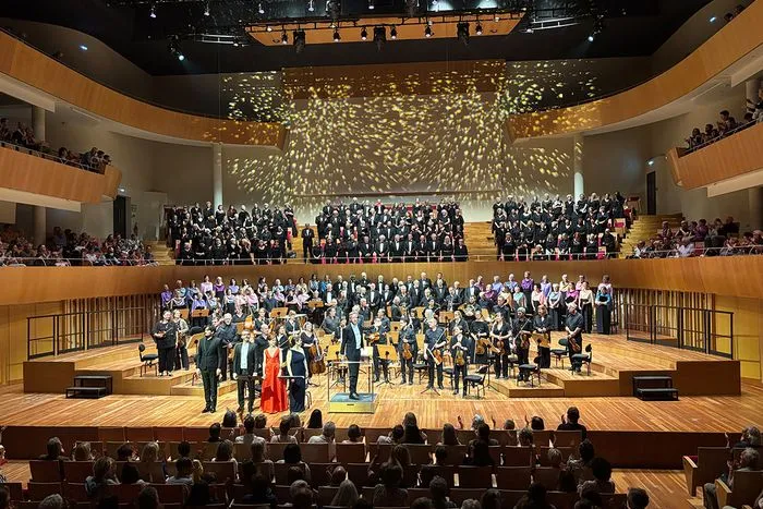 Concierto del coro sinfónico Viva Vivaldi en Burdeos con orquesta y cantantes en el escenario, público en balcones y platea de la sala de conciertos.