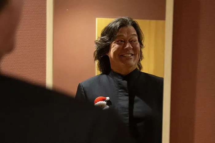Una mujer sonriente con chaqueta negra y una insignia de Papá Noel rojo y blanco en el Concierto de Navidad de Radio Classique en Burdeos