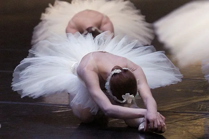 Bailarina de ballet con tutú blanco ejecutando una postura inclinada en el escenario durante una representación del Lago de los Cisnes en Burdeos