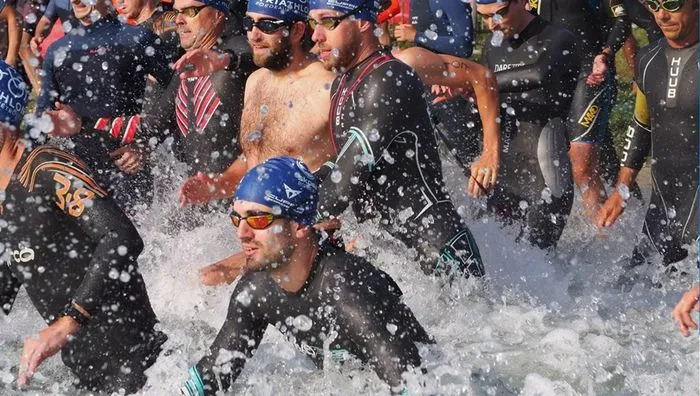 Grupo de triatletas saliendo del agua en el Triatlón de Burdeos, con salpicaduras visibles, nadadores equipados con trajes de neopreno y gafas de natación