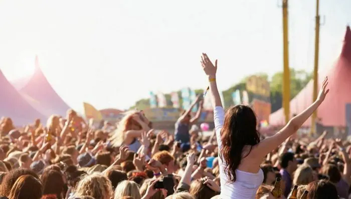 Multitud de espectadores levantando los brazos durante un concierto al aire libre en la Fiesta de la Música de Burdeos, con carpas rosas y estructuras visibles al fondo.