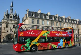 Un autobús turístico rojo de dos pisos del servicio Bordeaux Visiotour (Hop On Hop Off) estacionado frente a una torre medieval y edificios de estilo haussmann en Burdeos