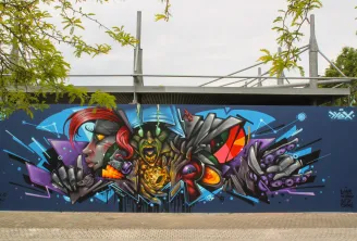 Mural de arte urbano colorido en el muro del M.U.R de Burdeos, con rostros estilizados y formas geométricas en azul, rojo, oro y púrpura sobre fondo azul oscuro, bajo un puente moderno.