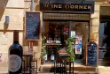 Fachada del Wine Corner, bar de vinos en Burdeos, con botellas de vino expuestas, terraza con mesas altas y carteles promocionales.