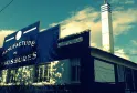 Fachada de La Manufactura en Burdeos, edificio industrial con letrero azul 'Manufactura de Calzado' y chimenea blanca bajo cielo azul despejado
