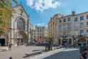 Plaza soleada en Burdeos con la iglesia de Saint-Pierre en primer plano, sus fachadas góticas ornamentadas y reloj, rodeada de edificios de estilo haussmanniano en piedra, con visitantes y terrazas de café.