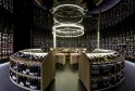 Bodega de vinos moderna del Latitude 20 Wine Bar en Burdeos, con estanterías curvas llenas de botellas, un mostrador central de madera e iluminación circular blanca en el techo.