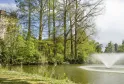 Vista del Parque de Bourran en Burdeos con una torre de piedra histórica, un lago con fuente, árboles majestuosos y exuberante vegetación primaveral.