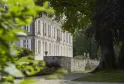 Vista del Château de La Dauphine en Burdeos con su fachada blanca de estilo clásico y columnas, rodeado de vegetación exuberante y árboles centenarios, accesible por escaleras de piedra.