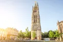 La Torre Pey-Berland, campanario gótico del siglo XV en Burdeos, con agujas ornamentadas y una estatua dorada en su cúspide, rodeada de edificios históricos y árboles.