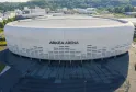 Vista aérea de la Arkea Arena, una arena moderna de formas redondeadas en blanco y gris, ubicada en Floirac cerca de Burdeos, con estacionamientos y explanada de acceso en primer plano.