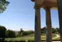 Vista desde una columnata de piedra del Parque Palmer en Burdeos, con césped verde, árboles y panorámica de la ciudad al fondo en día soleado.